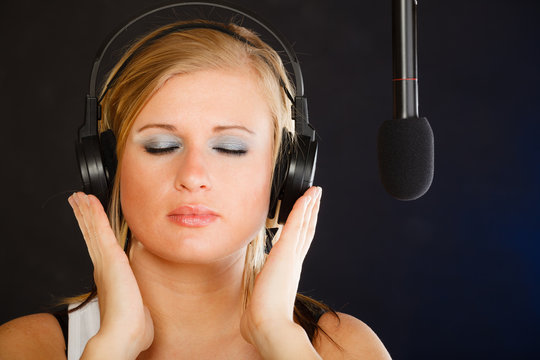 Woman singing to microphone wearing headphones in studio