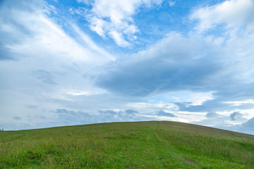 Fototapeta na wymiar Green grass hills landscape in summer against blue sky and white clouds.