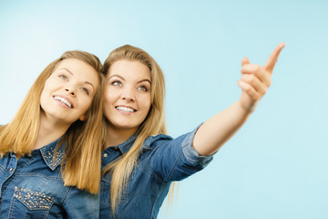 Two happy women friends wearing jeans outfit poitning