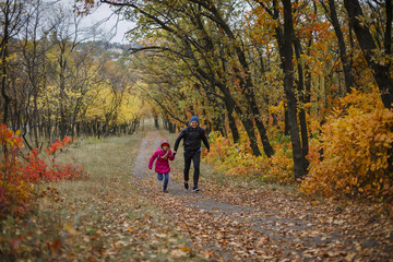 pretty little girl and young father walking in beautiful autumn park