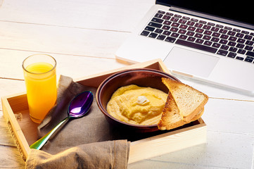 A sunny breakfast near the laptop. Polenta with butter and some crispy toast. Orange freshly squeezed juice and food on a tray for breakfast in bed.
