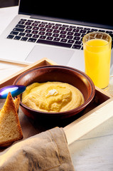 A sunny breakfast near the laptop. Polenta with butter and some crispy toast. Orange freshly squeezed juice and food on a tray for breakfast in bed.