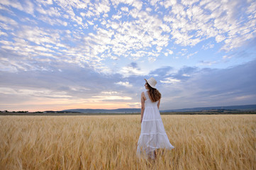 Fototapeta na wymiar Beautiful woman in a field of rye at sunset. A woman in amazing clothes walking through the field of rye.