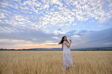 Beautiful woman in a field of rye at sunset. A woman in amazing clothes walking through the field of rye.