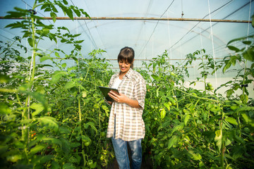Portrait of beautiful female farmer in a greenhouse using tablet