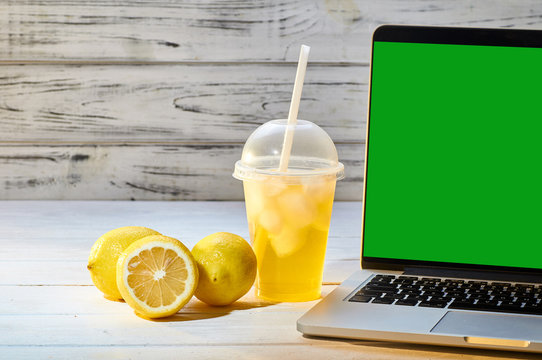 Refreshing drink with ice from lemons and other citrus. Alcoholic, non-alcoholic drink of bright yellow color on a white wooden table in the office. A break near the laptop at work.