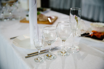 Glasses, flowers, fork, knife, napkin folded in a pyramid, served for dinner in restaurant with cozy interior. Wedding decorations and items for food, arranged by the catering service on a large table