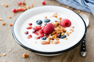 Yogurt with pomegranate, blueberry and granola in bowl on wooden table, selective focus. Healthy eating, healthy lifestyle concept