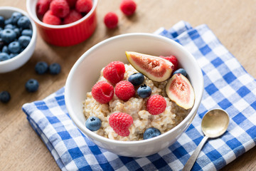 Oatmeal porridge with raspberries, blueberries and figs. Healthy breakfast food. Colofrul breakfast on a table