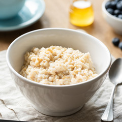 Oatmeal porridge, scottish oats in a bowl on table, kitchen linen. Healthy breakfast, healthy lifestyle concept. Square crop