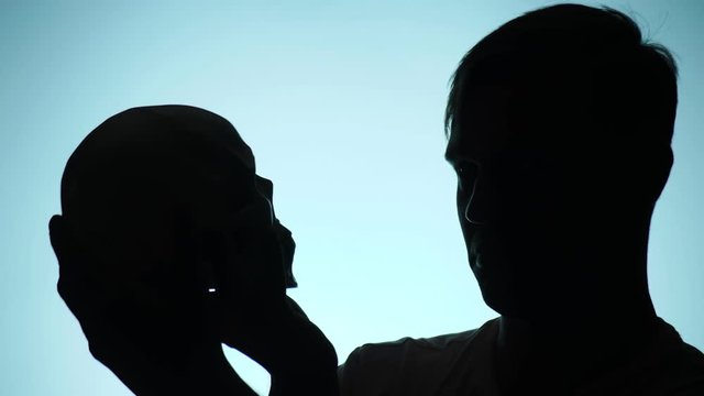 silhouette of man on blue background. funny man plays in the shadow theater. looks at the human skull 4k, slow motion