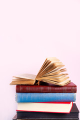 Stack of old books on shelf on pink background with copy space