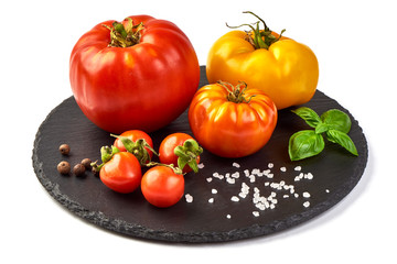 Fototapeta na wymiar Colorful yellow and red tomatoes of different sizes and kinds, on rustic slate stone plate, with spices an basil leaves, isolated on white background.