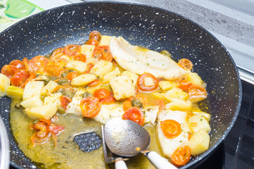 cod cooked in a pan, with tomato, potatoes and capers