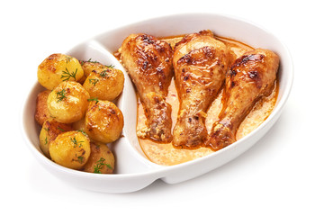 Appetizing baked chicken legs with cream sauce, potatoes and spices on white background.