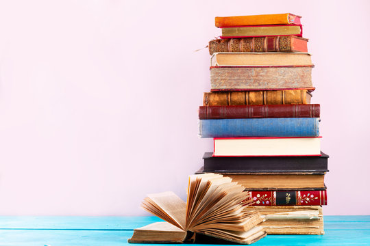 Pile of vintage books on blue wooden shelf, copy space on pink wall background