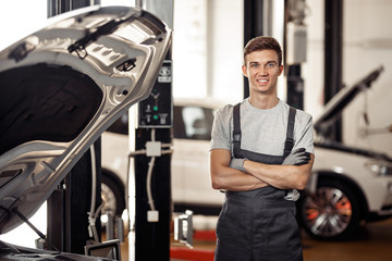 A young and qulified automechanic is standing near the car at a 