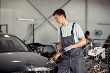 A young mechanic is washing a black car at his work at a car service
