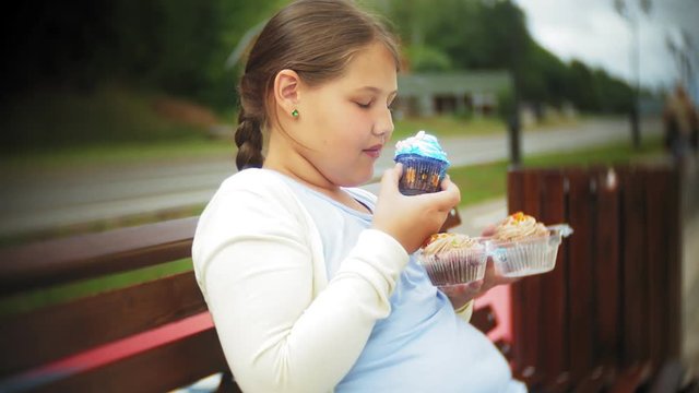 Close up of adorable little fat girl eating vegetables with her hands sitting on a bench in the park, concept of healthy eating