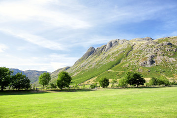 The Langdale Valley in the picturesque Lake District in the UK england, featuring the Langdale Pikes set against a deep blue summer sky with green fields. A perfect English landscape 