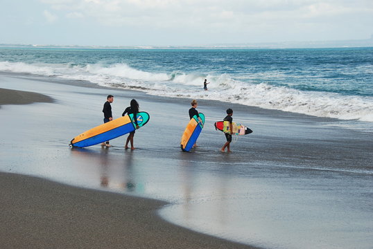 Surfers with surf boards on the Pantai Batu Bolong Beach going into the sea with huge waves, south Bali, Indonesia 