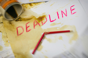 Deadline written on paper in red on the background of spilled coffee and a broken pencil.