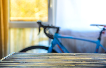 Empty Wooden Table in Front of Blurred Background of Living Room with a Blue Bicycle Near the Window. Mock Up for Display of Product. Blank for Your Layout