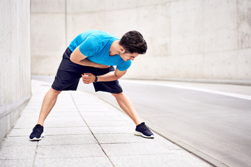 Athletic man bending forward doing exercises during urban workout session