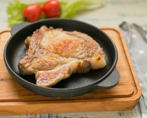 A piece of fried meat in a frying pan on a light wooden background.