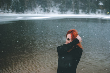 Snowflakes flying over handsome black-eyed redhead girl looking at the camera and playing with her beautiful hair. Closeup of falling snowflakes. 