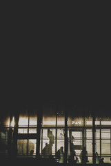 Black sillhouettes of people waiting for their train on a subway station behind glass windows filled with sunshine