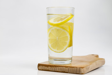 A glass of cold water with lemon on a white kitchen table. A refreshing drink in warm weather.