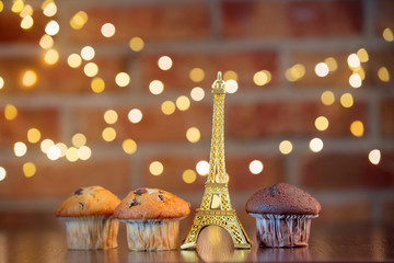Homemade classic and chocolate cupcakes and Eiffel tower souvenir. Fairy lights and gift box in bokeh background. Christmas time concept