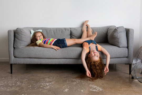 Playful little girls lying on grey sofa