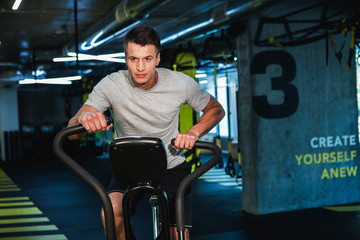 Fototapeta na wymiar Motivated man is warming-up before powerful workout in gym. He is feeling strained while running on elliptic machine. Training with simulators concept