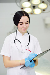 young pretty doctor girl in white medical dressing gown with stethoscope on modern clinic background
