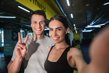 Portrait of satisfied man and woman taking their own photo after workout. Smiling girl is holding...