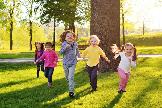 a group of small happy children run through the park in the background of grass and trees. Children's outdoor games, vacations, weekend, Children's Day, June 1