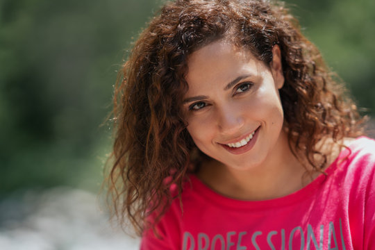 Close up portrait of a cheerful curly young woman smiling outdoors