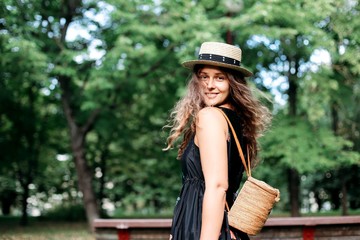 long-haired smiling travel girl with a straw backpack and hat on nature.