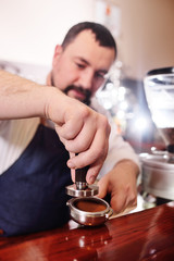 a handsome, bearded barista man holding a Holder with ground coffee. Making coffee in a coffee house