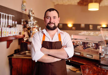 portrait of a handsome male barista in an apron on the background of a cozy coffee house and a coffee machine.