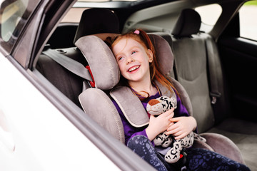 happy cheerful baby girl sitting with toy in car seat and smiling
