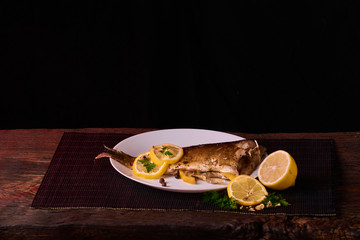 Grilled fish with herbs and lemon on wooden background. Mediterranean luxurious seafood concept