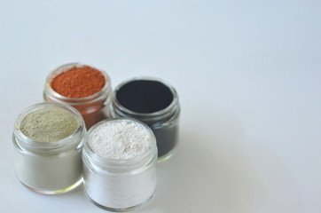 Top view of kaolin powder, activated charcoal, red, green and green cosmetic clays in jars. Deep cleansing bentonite (montmorillonite) clay for beauty spa face mask, body detox and hair treatments. 