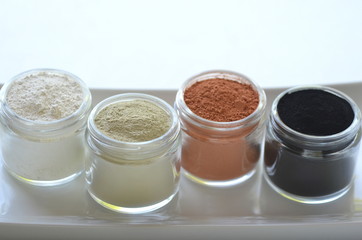 Top view of kaolin powder, activated charcoal, red, green and green cosmetic clays in jars. Deep...