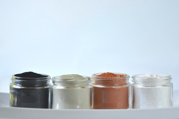 front view of glass jars with cosmetic red green clay powder, kaolin and activated charcoal for face masks. Deep cleansing bentonite (montmorillonite) clay for body detox and hair treatments.
