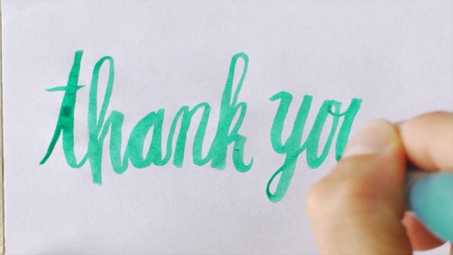 Hand writing the words THANK YOU in cursive with a green pen