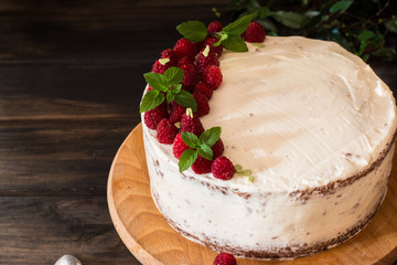 Portion of layered creamy fruit cake with in close up view. Raspberry cake with chocolate. Chocolate cake. Mint decoration. Cheesecakeon wooden table and dark background. Still life of food.