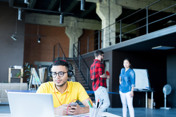 Portrait of  creative young Middle-Eastern man wearing headphones and bright yellow shirt using...